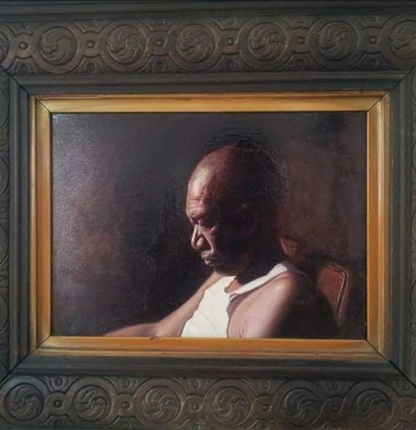 Framed oil portrait of a seated man in warm, low light